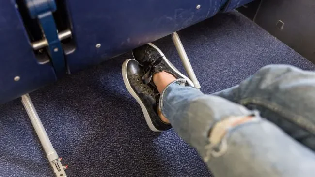 Crossed legs in cramped airplane legroom under the seat in front